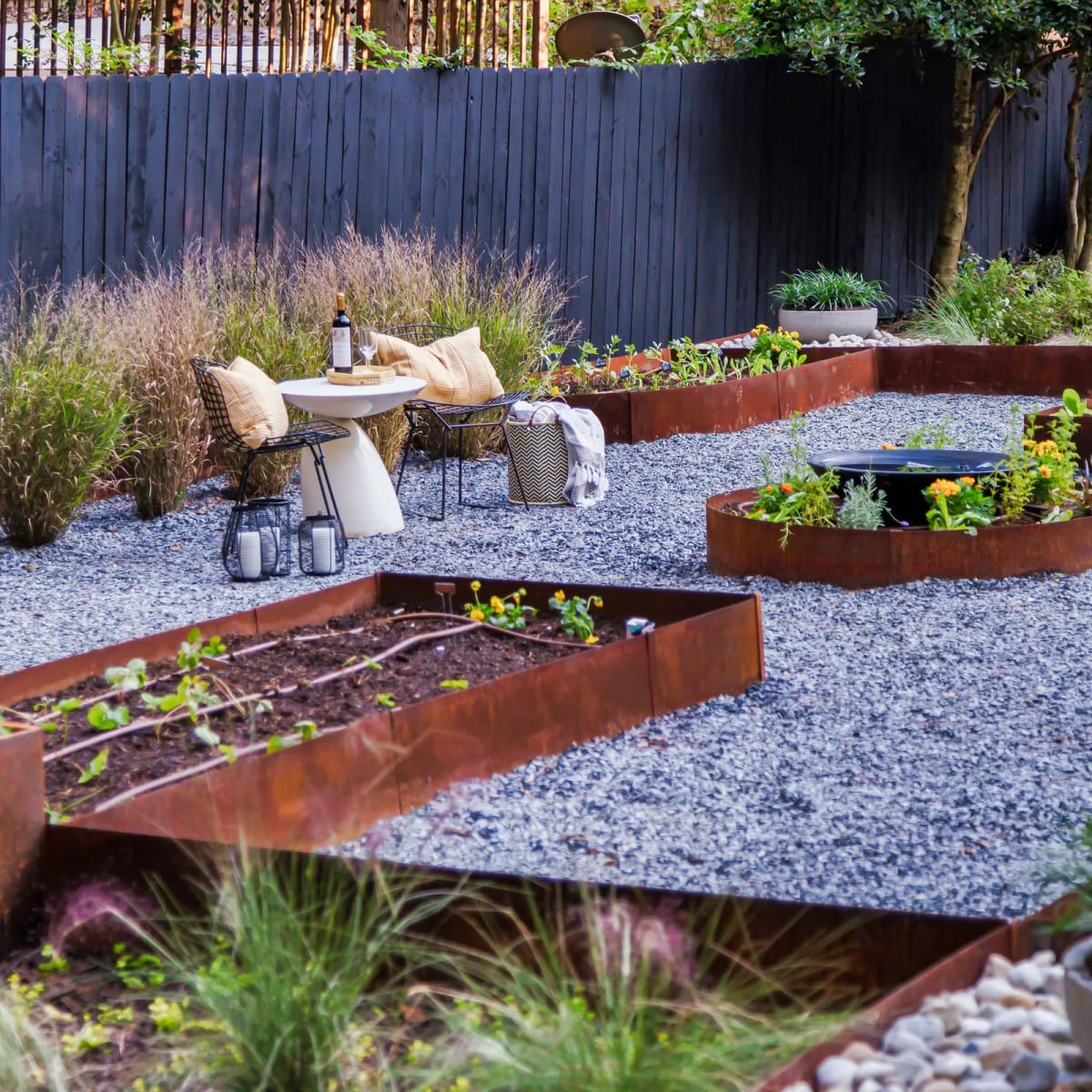 Weathered steel borders curve through a garden with gravel paths, planted beds, and a seating area